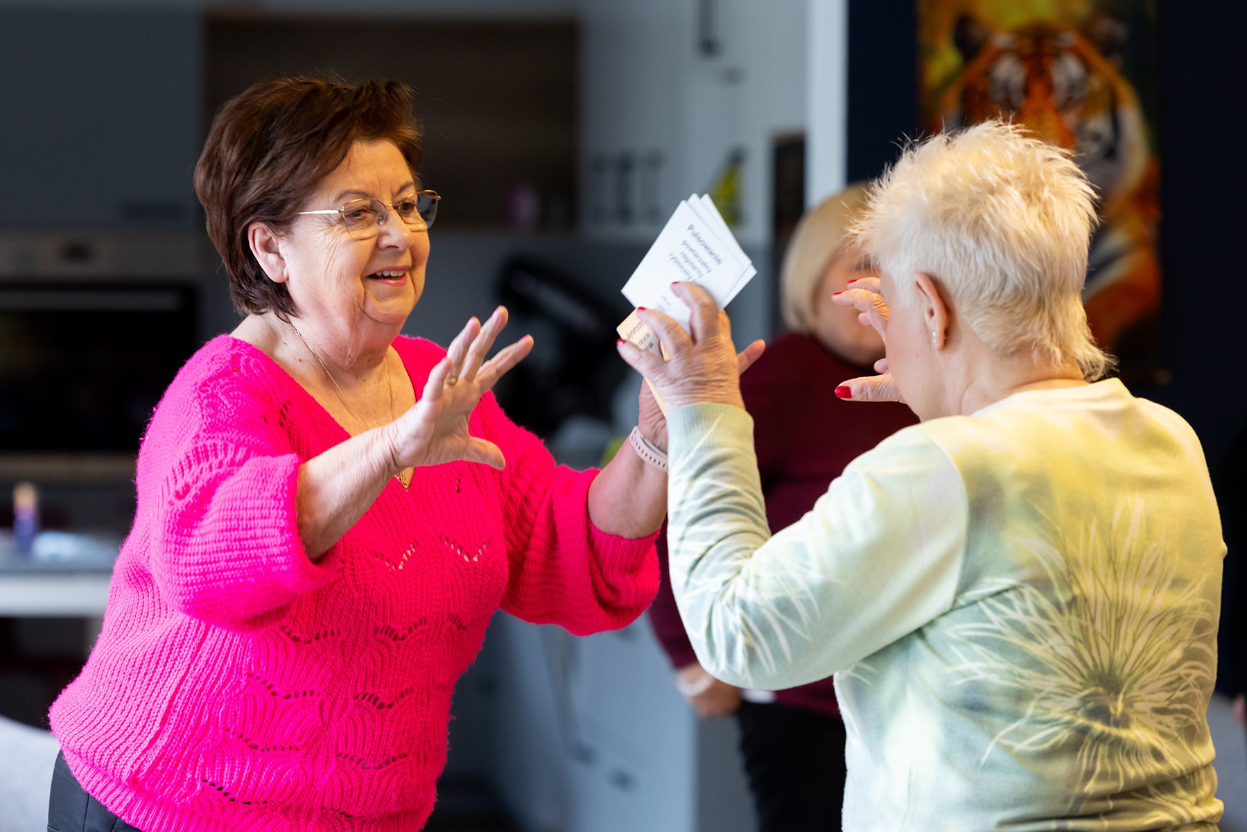 Dwie starsze kobiety w pomieszczeniu stoją naprzeciwko siebie i łapią nieistniejącą piłkę