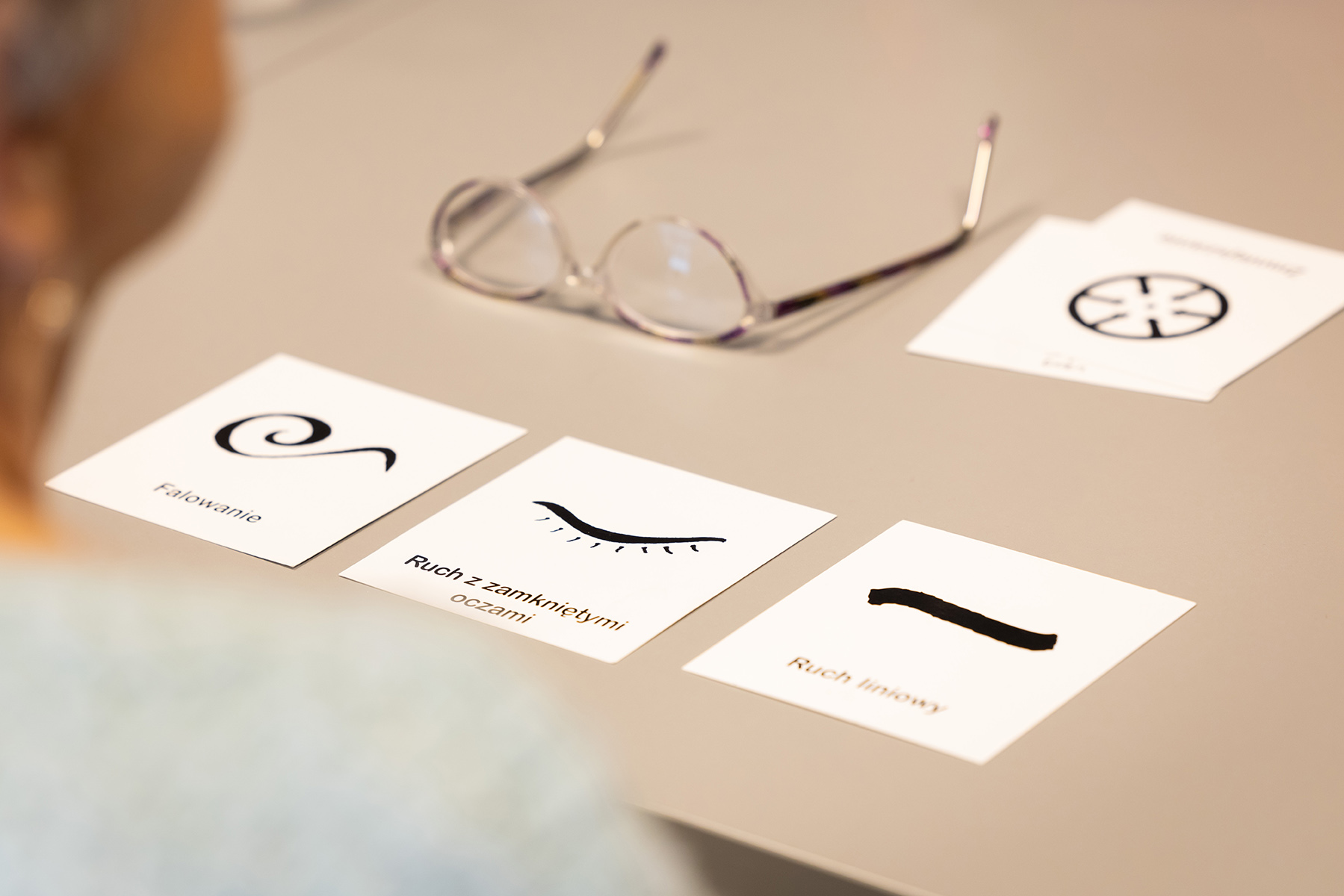 Na stole leżą okulary i cztery kwadratowe karty z symbolami i podpisami